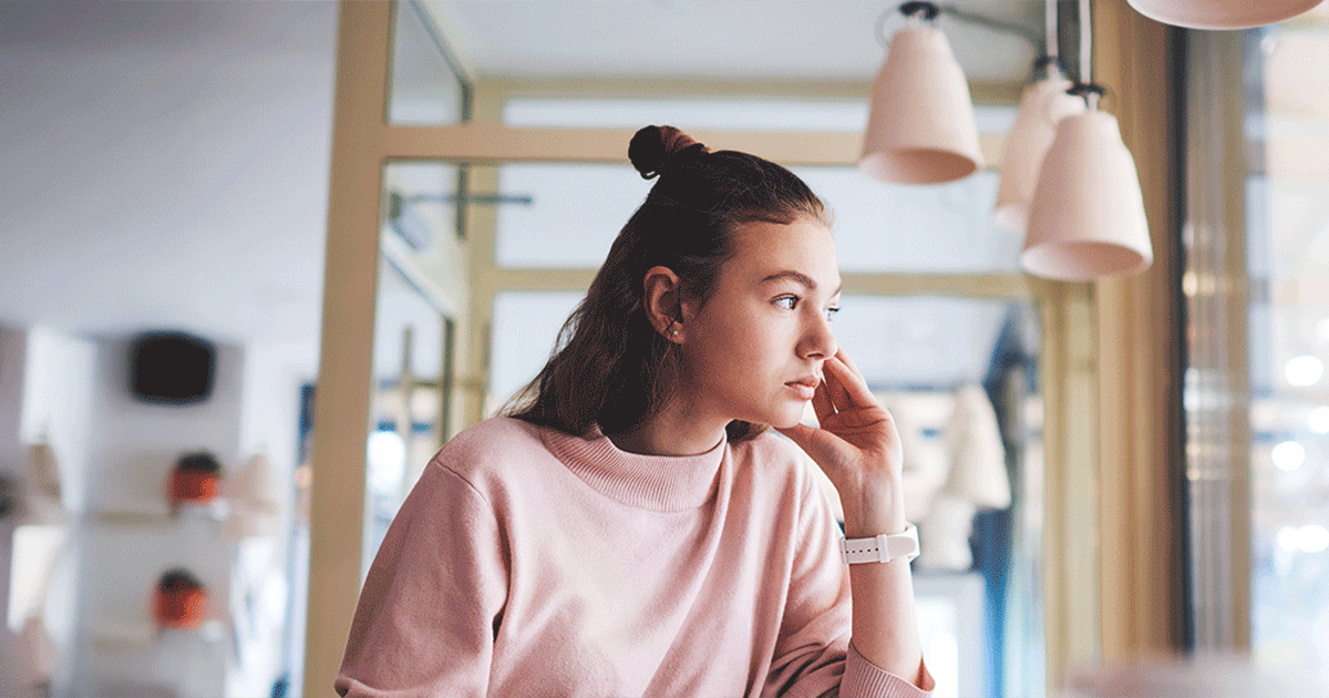 Woman looking out a window while considering how to navigate an unexpected pregnancy between jobs.